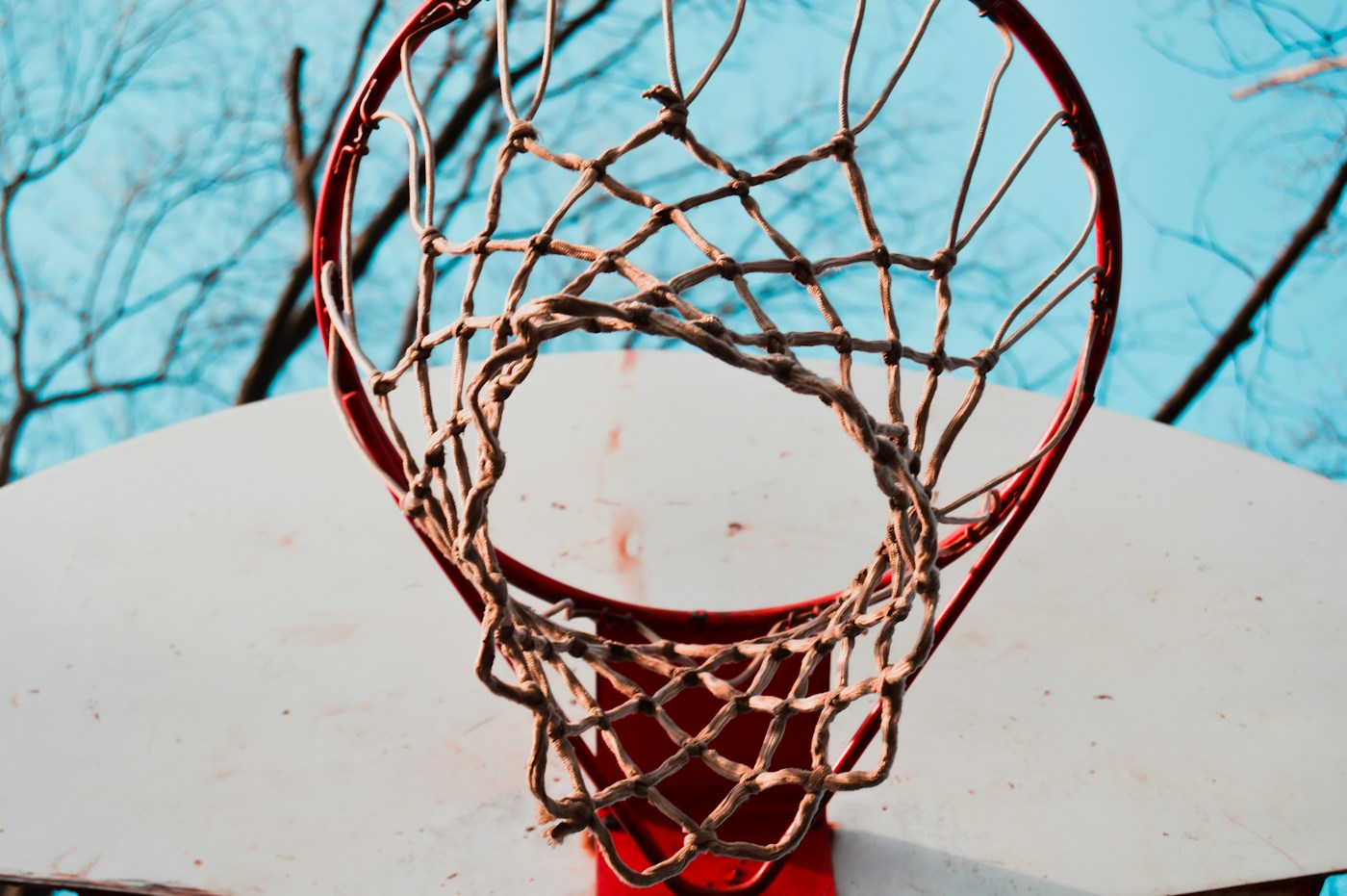 Looking up through a red rim and worn net at a bright sky